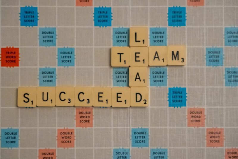 Tiles on a Scrabble board that are connected together and spell the words Lead, Team, and Succeed