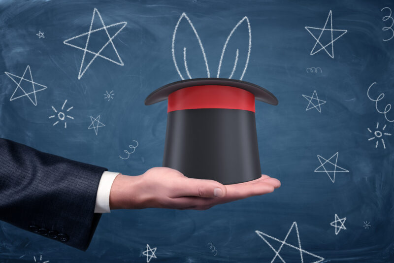 A businessman's hand holding a magicians hat with chalk drawn rabbit ears sticking outside of it.